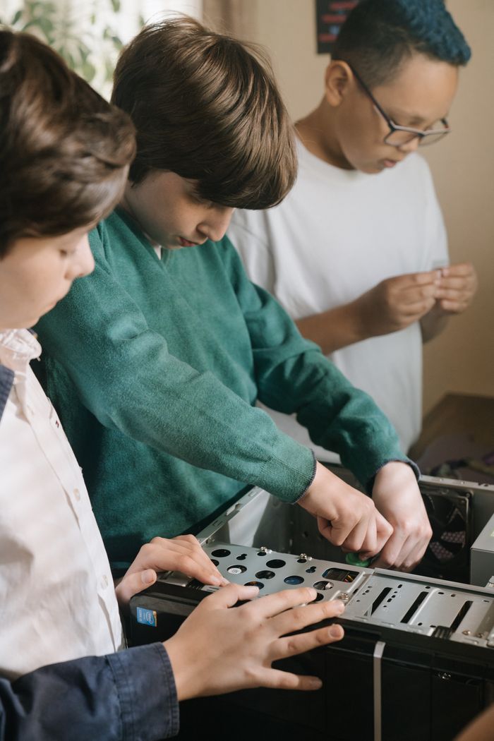 Three children assembling a desktop computer indoors, showcasing teamwork and technology skills.