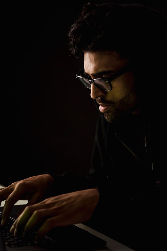 Side view of attentive ethnic cyber spy in eyeglasses typing on netbook at table in evening